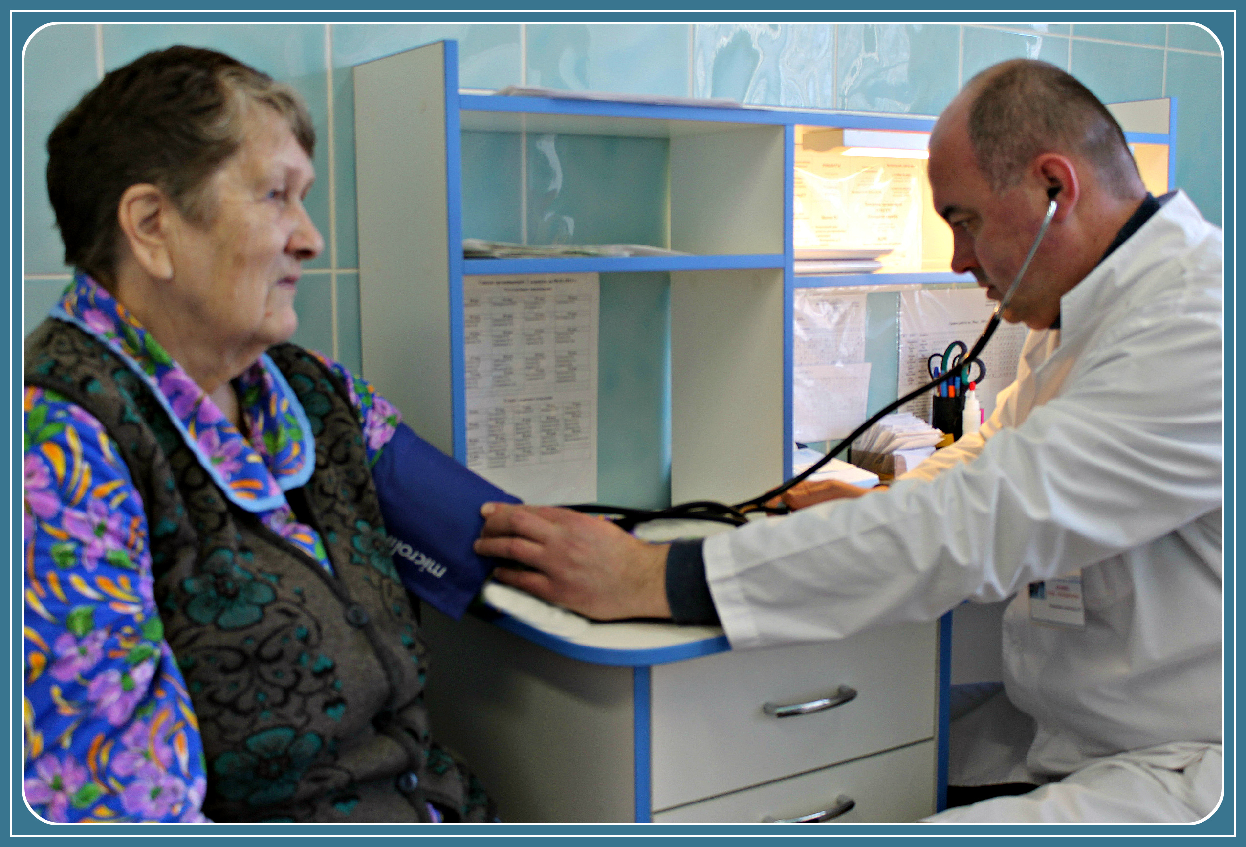Заведующий отделением милосердия Коржев Р.В. измеряет артериальное давление получателю социальных услуг на посту дежурной медсестры.
