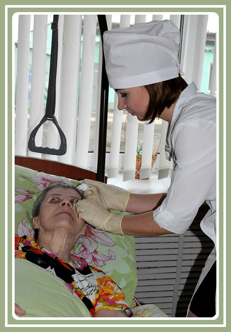 Медсестра закапывает глаза получателю социальных услуг непосредственно в ее в комнате.